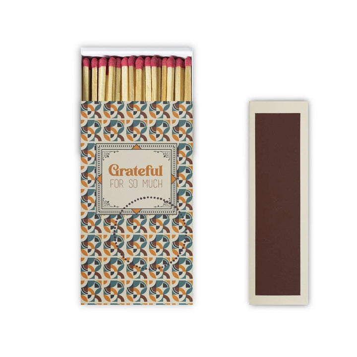 A matchbox with a matte finish design containing red safety matches, with text 'GRATEFUL FOR SO MUCH' on the packaging.