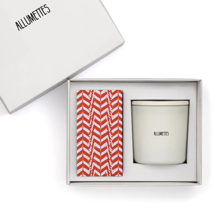 A white candle from Allumettes placed in a gift box with a red and white patterned matchbox.